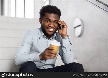 business, technology, communication and people concept - african american businessman calling on smartphone and drinking coffee at office stairs. businessman calling on smartphone at office stairs. businessman calling on smartphone at office stairs