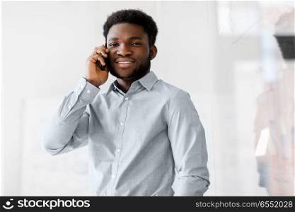 business, technology, communication and people concept - african american businessman calling on smartphone at office glass board. businessman calling on smartphone at office. businessman calling on smartphone at office