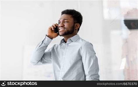 business, technology, communication and people concept - african american businessman calling on smartphone at office glass board. businessman calling on smartphone at office. businessman calling on smartphone at office