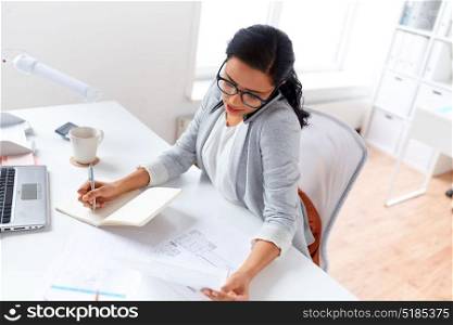 business, technology, communication and people concept - businesswoman or secretary calling on smartphone and writing to notebook at office. businesswoman calling on smartphone at office