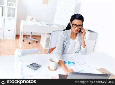business, technology, communication and people concept - businesswoman with laptop computer papers calling on smartphone at office. businesswoman calling on smartphone at office