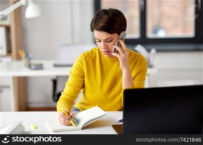 business, technology, communication and people concept - businesswoman with pen and notebook calling on smartphone at office. businesswoman calling on smartphone at office