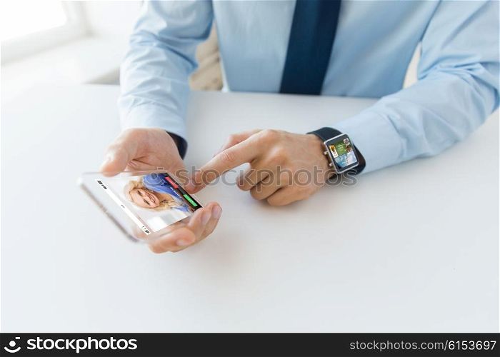 business, technology, communication and people concept - close up of male hand holding and showing transparent smart phone and watch at office with incoming call on screen