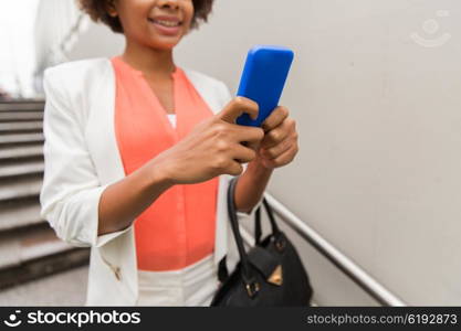 business, technology, communication and people concept - close up of young smiling african american businesswoman with smartphone and handbag texting walking downstairs to city subway