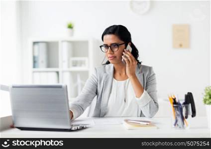 business, technology, communication and people concept - happy businesswoman with laptop computer calling on smartphone at office. businesswoman with laptop and smartphone at office