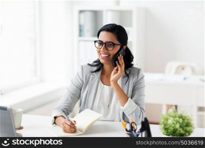 business, technology, communication and people concept - happy smiling businesswoman or secretary with notebook calling on smartphone at office. businesswoman calling on smartphone at office