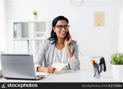 business, technology, communication and people concept - happy smiling businesswoman or secretary with notebook calling on smartphone at office. businesswoman calling on smartphone at office