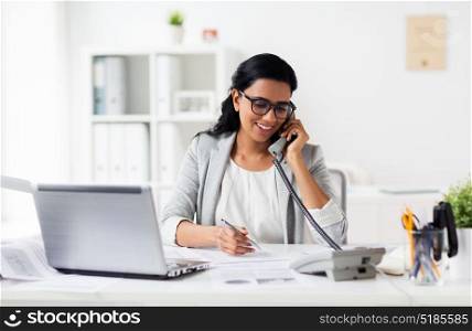business, technology, communication and people concept - happy smiling businesswoman with papers calling on phone at office. happy businesswoman calling on phone at office