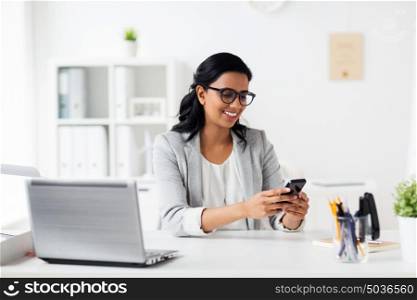 business, technology, communication and people concept - happy smiling businesswoman with smartphone and laptop at office. businesswoman with smartphone and laptop at office