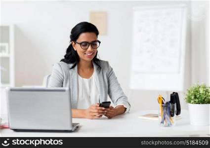business, technology, communication and people concept - happy smiling businesswoman with smartphone and laptop at office. businesswoman with smartphone and laptop at office