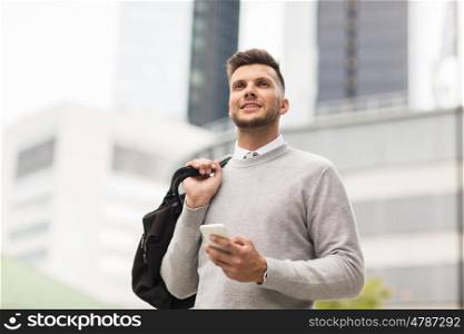 business, technology, communication and people concept - happy smiling young man in with bag and smartphone on city street