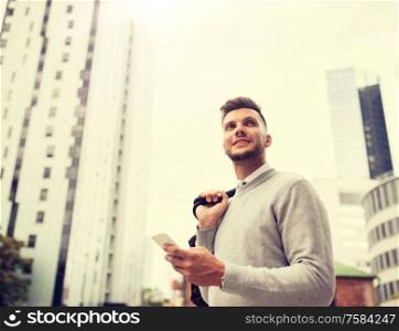 business, technology, communication and people concept - happy smiling young man with bag and smartphone on city street. happy young man with bag and smartphone in city