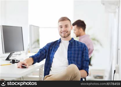 business, technology, communication and people concept - happy young creative man or student with computer and smartphone at office