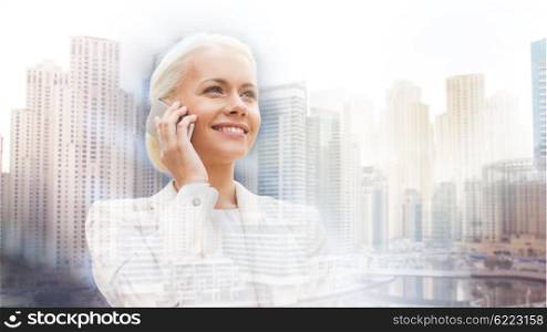 business, technology, communication and people concept - smiling businesswoman with smartphone talking over dubai city background with double exposure effect