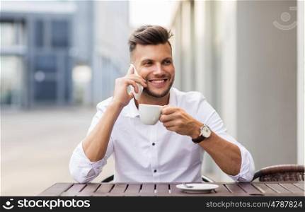 business, technology, communication and people concept - smiling young man drinking coffee and calling on smartphone at city street cafe