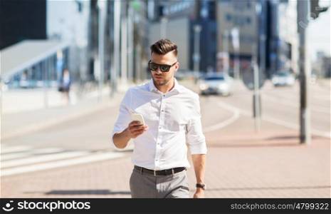 business, technology, communication and people concept - young man in sunglasses with smartphone walking in city