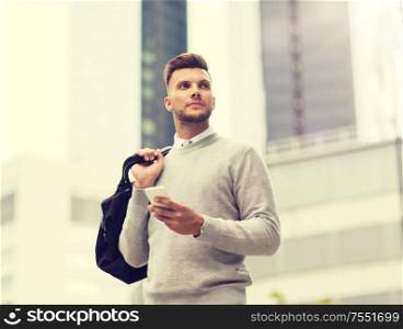 business, technology, communication and people concept - young man in with bag and smartphone on city street. young man with smartphone and bag in city