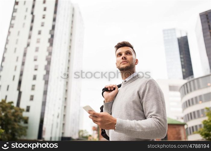 business, technology, communication and people concept - young man with bag and smartphone on city street