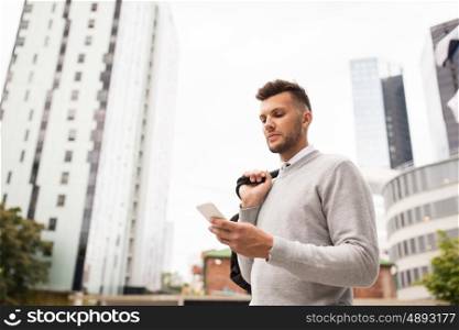 business, technology, communication and people concept - young man with bag texting on smartphone on city street