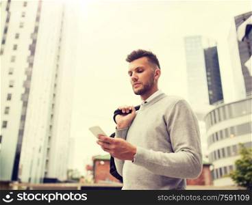 business, technology, communication and people concept - young man with bag texting on smartphone on city street. young man with bag texting on smartphone in city