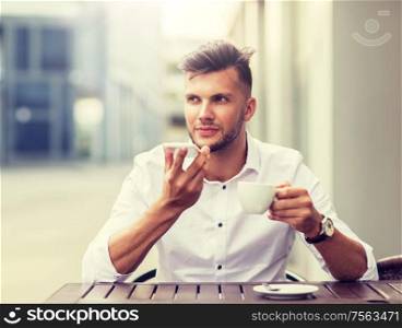 business, technology, communication and people concept - young man with coffee using voice command recorder on smartphone at city street cafe. man with coffee and smartphone at city cafe