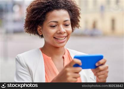 business, technology, communication and people concept - young smiling african american businesswoman with smartphone reading message on city street