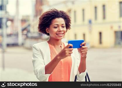 business, technology, communication and people concept - young smiling african american businesswoman with smartphone reading message on city street