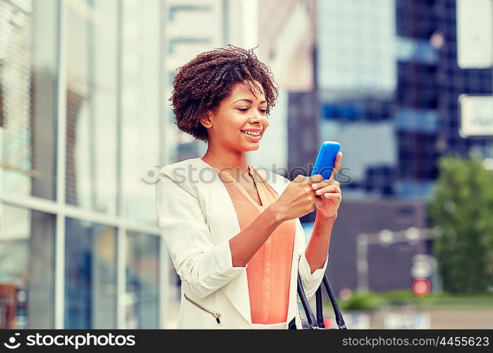 business, technology, communication and people concept - young smiling african american businesswoman with smartphone in city