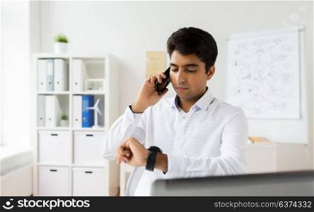 business, technology, communication and punctuality concept - close up of businessman calling on smartphone and looking at his wristwatch at office. businessman calling on smartphone at office