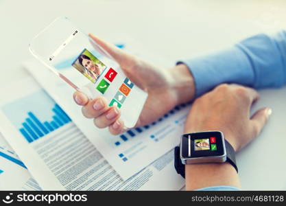 business, technology, communication, connection and people concept - close up of woman hand holding transparent smartphone and smartwatch with incoming call at office