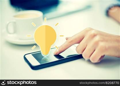 business, technology, communication, idea and people concept - close up of woman hand pointing finger to smartphone screen with lighting bulb icon in office