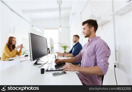 business, technology, design and people concept - young creative man or designer with computer and pen tablet working at office