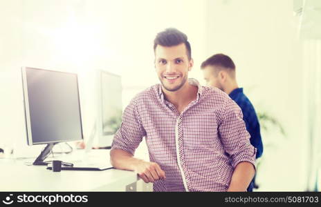 business, technology, education and people concept - happy young creative man or student with computer at office. happy creative man with computer at office
