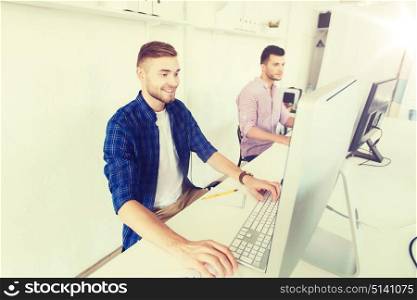 business, technology, education and people concept - happy young creative man or student with computer at office. creative man or student with computer at office