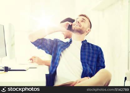 business, technology, education and people concept - happy young creative man or student with computer at office calling on smartphone. happy creative man calling on cellphone at office