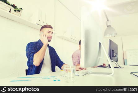 business, technology, education and people concept - happy young creative man or student with computer at office calling on smartphone. happy creative man calling on cellphone at office