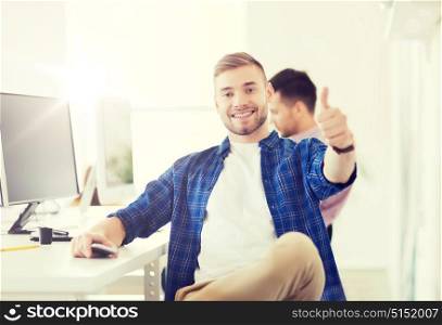 business, technology, education and people concept - happy young creative man or student with computer at office at office showing thumbs up. happy creative man with computer at office