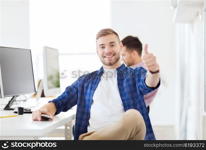 business, technology, education and people concept - happy young creative man or student with computer at office at office showing thumbs up