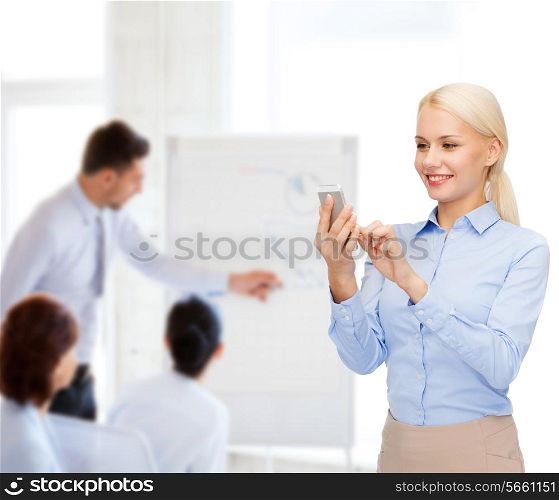 business, technology, education and people concept - smiling young businesswoman with smartphone in office
