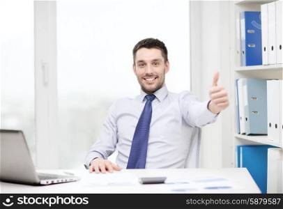 business, technology, finances and internet concept - smiling businessman with laptop computer and documents at office showing thumbs up
