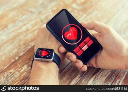 business, technology, health care and people concept - close up of male hand holding smart phone and wearing smart watch showing red heart beat icon on screen