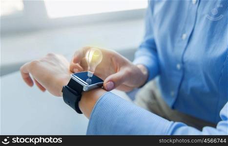 business, technology, idea, startup and people concept - close up of woman hands setting smart watch with light bulb projection at office