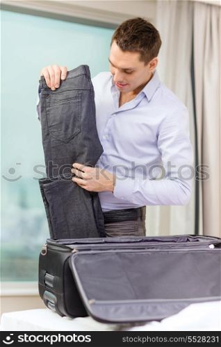 business, technology, internet and hotel concept - happy businessman packing things in suitcase in hotel room