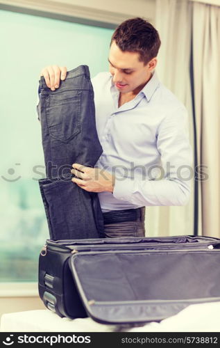 business, technology, internet and hotel concept - happy businessman packing things in suitcase in hotel room