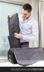 business, technology, internet and hotel concept - happy businessman packing things in suitcase in hotel room