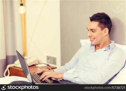 business, technology, internet and hotel concept - happy businessman with laptop computer lying in hotel in bed