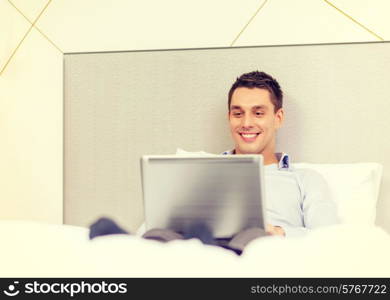 business, technology, internet and hotel concept - happy businessman with laptop computer lying in hotel in bed