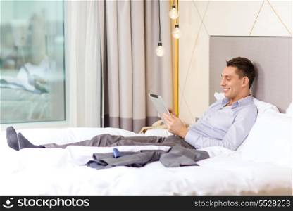 business, technology, internet and hotel concept - happy businessman with tablet pc computer lying in hotel in bed