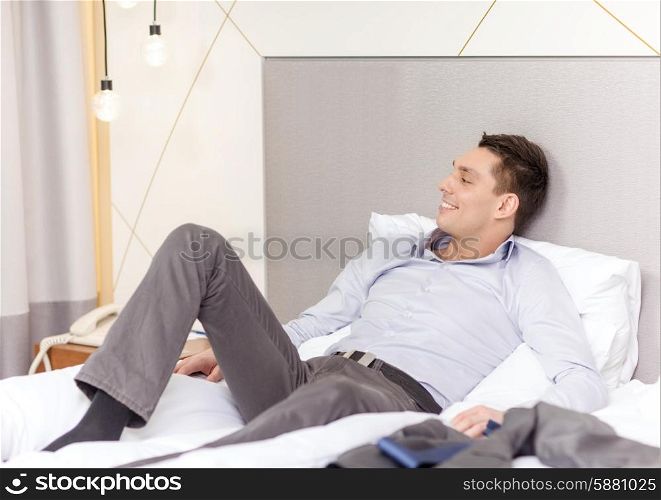 business, technology, internet and hotel concept - happy businesswoman lying in bed in hotel room