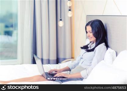 business, technology, internet and hotel concept - happy businesswoman with laptop computer lying in hotel in bed